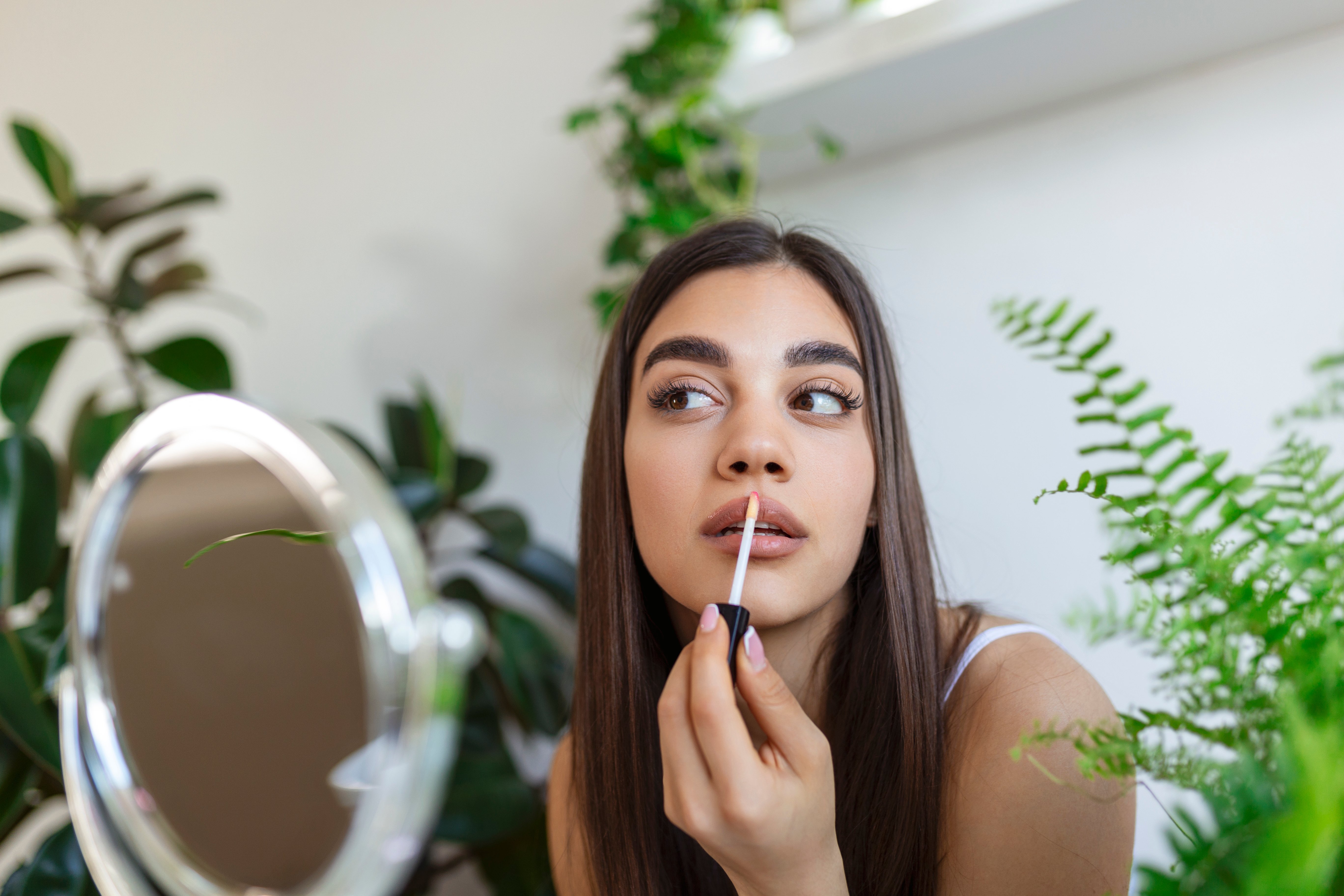 beautiful-young-woman-applying-lip-gloss-with-applicator-front-mirror-home